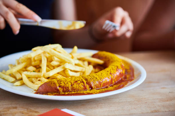 deutsche currywurst mit pommes wird von einer jungen frau gegessen - currywurst stock-fotos und bilder