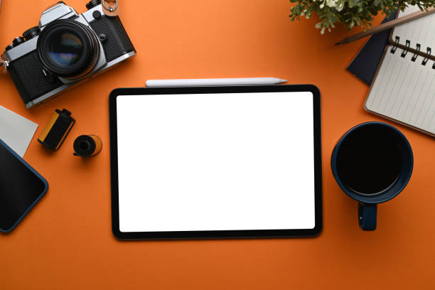 istock Top view of mock up digital tablet, camera, coffee cup and notebook on orange background. 1311763416