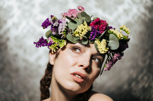 Studio portraits of a woman in her thirties wearing natural flowers in her head and the hair with a braid. She poses with different facial expressions, sometimes looking towards the camera. The backdrop is unfocused, the images have low depth of field.