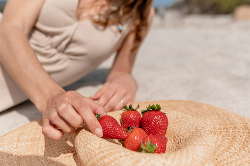 Close-up strawberries on a straw hat and blurred unrecognizable woman on background lying on the beach.