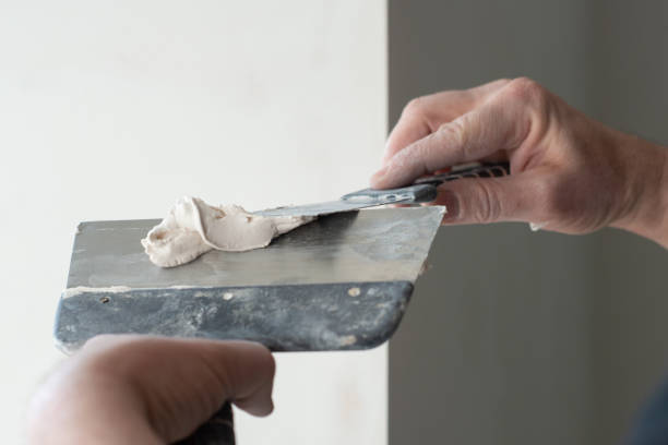 istock Worker putts plasterboard ceiling in new apartment. Repairman works with plasterboard, plastering dry-stone wall, home improvement. A man makes repairs at house. Putty knife in male hand. Hand work. 1311778911