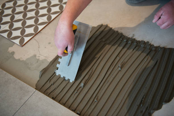 tiler posa la piastrella di ceramica sul pavimento. il lavoratore professionista effettua lavori di ristrutturazione. costruzione. mani del tiler. ristrutturazione della casa e costruzione di una nuova casa - plaster plasterer wall repairing foto e immagini stock