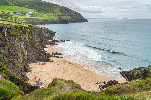 People swimming in turquoise coloured see and families relaxing on Coumeenoole Beach hidden between cliffs, Dingle, Wild Atlantic Way, Kerry, Ireland