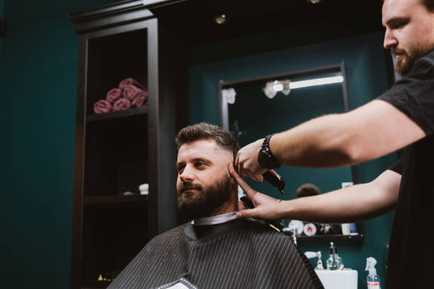 istock Barber using hair clipper to do haircut for male client 1311788497