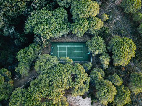 Aerial view of a tennis court surrounded by nature. Green color. Many trees against the tennis/soccer sport court.