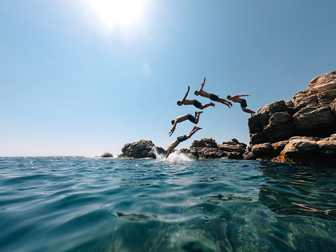 Millennial man is diving from a rock in the sea - Multiple images effect. Italy - Mediterranean sea during summer.