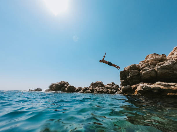 l’homme millénaire plonge d’un rocher dans la mer - spraying beaches summer sunlight photos et images de collection