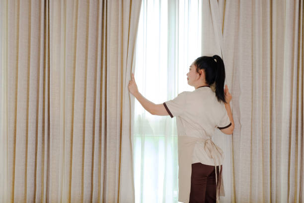 istock Young maid opening curtains in hotel room 1311791286