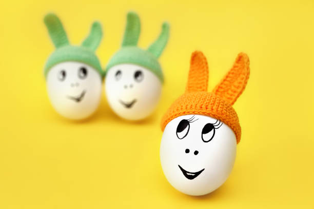 istock funny egg in orange cap with ears on yellow background and two eggs in green caps 1311793511