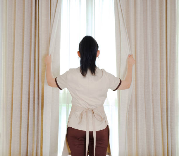 istock Young maid opening curtains in hotel room 1311793648