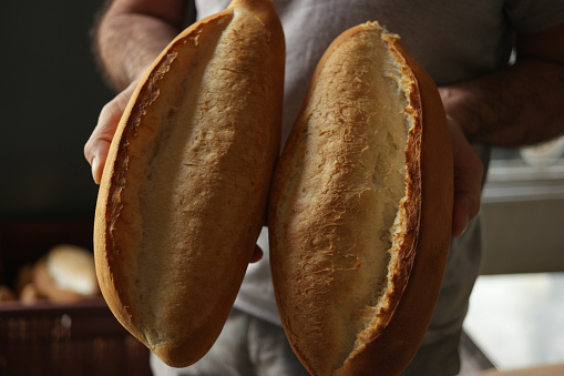 Hands of chef baker holding two loaves of fresh baked bread. Delicious natural food.