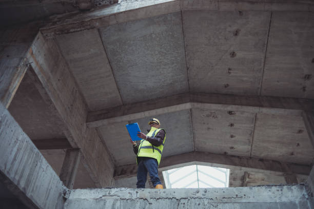 porträt von ingenieur-leseplänen auf der baustelle. ein bauingenieur mit einem schutzhelm, der eine sicherheitsweste trägt, verwendet ein digitales tablet. arbeiten an gebäudeanpassungen und investitionsbewertungen. - business ceo building activity business person stock-fotos und bilder