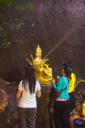 Thai women are praying at golden buddhist hindu statue on  Khao Khitchakut in night. Capture from behind people. Khao Khitchakut is only temporarily opened mountain area with shrine and buddha's footprint