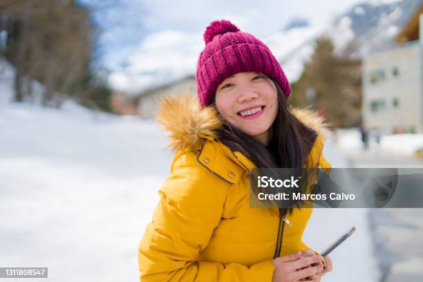 Winter Holidays In Swiss Alps Young Beautiful And Happy Asian Chinese Woman Holding Mobile Phone On Snow Landscape Smiling Cheerful In The Cold Mountainn Stock Photo - Download Image Now