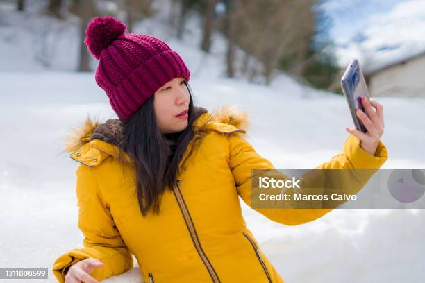 Winter Holidays In Swiss Alps Young Beautiful And Happy Asian Chinese Woman Holding Mobile Phone On Snow Landscape Smiling Cheerful In The Cold Mountainn Stock Photo - Download Image Now