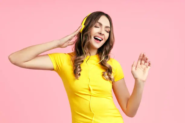 Photo of Cheerful young woman listening to music with headphones and dancing