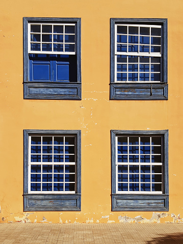 Fragment of the old facade with closed vintage windows. Traditional guillotine windows front view. Four old style blue wooden windows on a bright orange wall. Construction, architecture pattern.