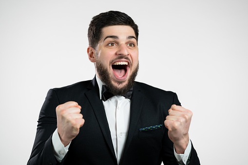 Businessman in tuxedo is very glad and happy, he shows yes gesture of victory, guy achieved result, goals. Surprised excited happy bearded guy on white background. High quality photo