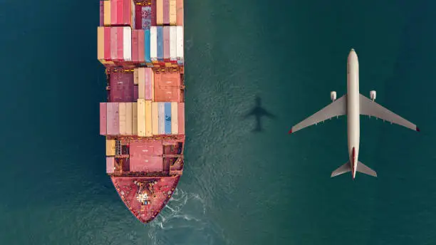 Photo of Cargo airplane flying over container ship in the ocean.