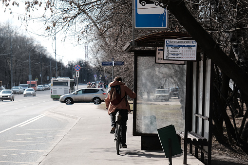 Moscow, Russia - April 10, 2021: Man is riding a bicycle next to a bus stop on city street