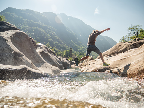 Hiker male jumps over the river from rock to rock. Springtime.
Ticino