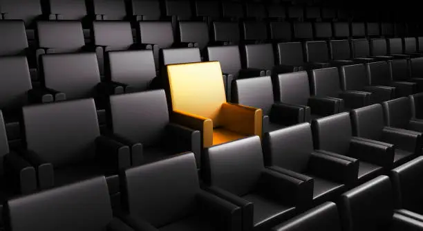 One golden seat in an empty auditorium surrounded by rows of black seats