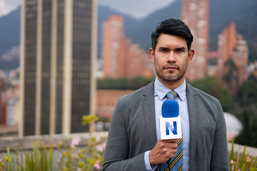 Portrait of a Latin American tv reporter outdoors reporting breaking news and looking at the camera - The Media concepts. **LOGO DESIGN WAS MADE FROM SCRATCH BY US**