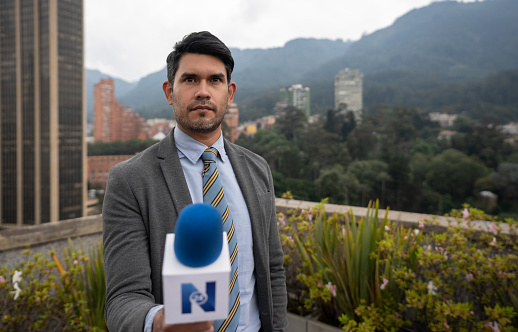 Portrait of a Latin American journalist interviewing a person outdoors for the news and holding the microphone - POV concepts. **LOGO DESIGN WAS MADE FROM SCRATCH BY US**