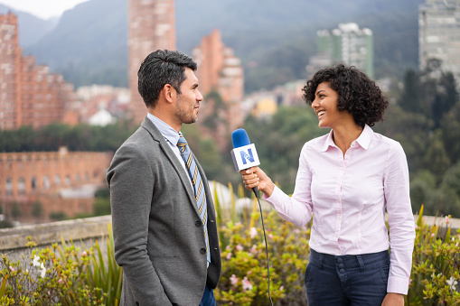 Happy Latin American female journalist outdoors interviewing a business man for the news - The Media concepts. **LOGO DESIGN WAS MADE FROM SCRATCH BY US**