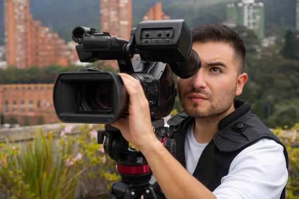 Cameraman outdoors recording breaking news Portrait of a Latin American cameraman outdoors recording breaking news - The Media concepts camera operator stock pictures, royalty-free photos & images