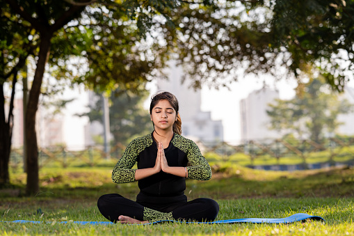 Outdoor image of young Woman doing yoga and meditating in prayer position at park.