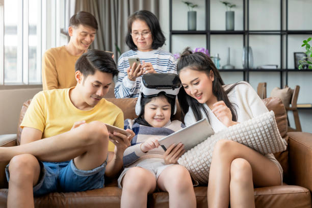 tecnologia intelligente con stile di vita a casa, la famiglia di generazione asiatica gode di dispositivi tecnologici uso a mano tablet smartphone e occhiali vrggle giocare divertimento insieme sul soggiorno divano nel momento della quarantena a casa - ipad television digital tablet connection foto e immagini stock