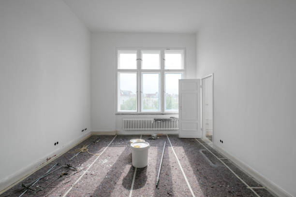 Painting in a white room with windows with a stepladder and paints on the floor.