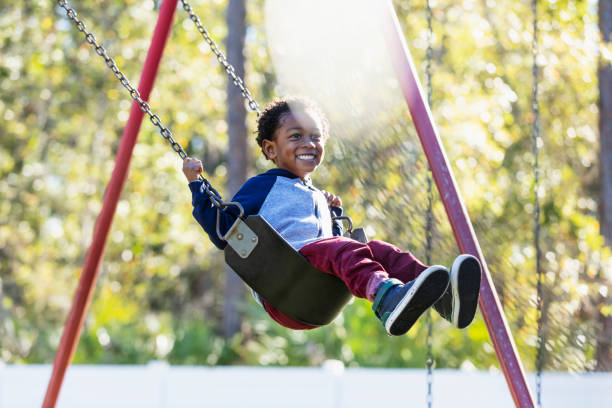Little boy on playground swing A little boy having fun swinging on a swing on the playground. He is 3 years old, mixed race Hispanic, African-American and Native American. swing stock pictures, royalty-free photos & images