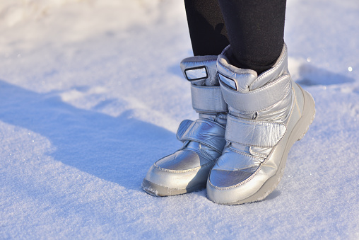 Children's winter boots in silver color on the snow.