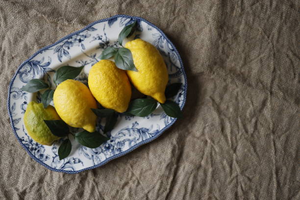 istock Lemons and artificial green leaves on white ceramic plate with blue floral pattern on burlap fabric 1311827227