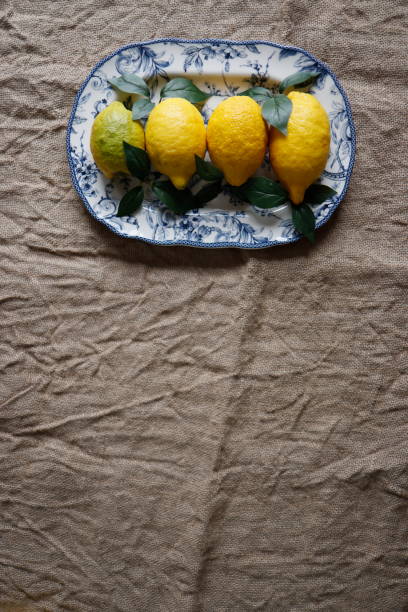 istock Lemons and artificial green leaves on white ceramic plate with blue floral pattern on burlap fabric 1311827284