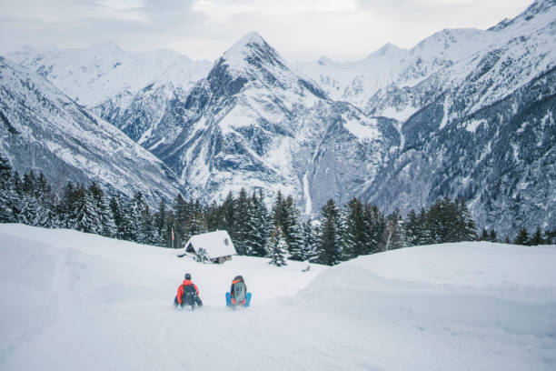 joven pareja toboggan por la pendiente de nieve en la mañana - mountain cabin european alps switzerland fotografías e imágenes de stock