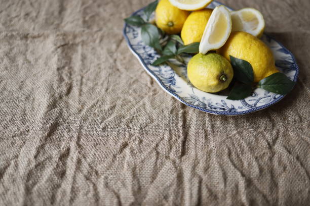 Lemons and lemon slices and artificial green leaves on white ceramic plate with blue floral pattern on burlap fabric
