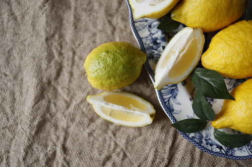 Istanbul, Turkey-March 20, 2021: Lemons and lemon slices and artificial green leaves on white ceramic plate with blue floral pattern on burlap fabric. Lemons on a rectangular serving plate. Still life, Full Frame, Sunlight. Shot with Canon EOS R5.