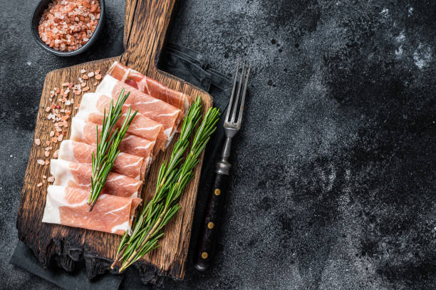 jamón prosciutto crudo parma, carne de cerdo curada seca en una tabla de madera. fondo negro. vista superior. copiar espacio - jamón de parma fotografías e imágenes de stock