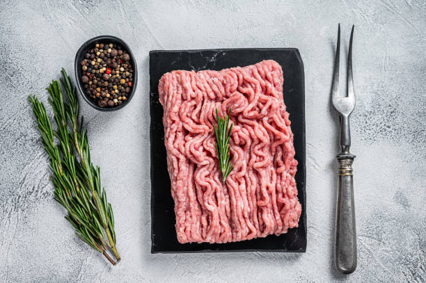 istock Minced chicken or turkey raw meat on cutting board with herbs. White background. Top View 1311830353