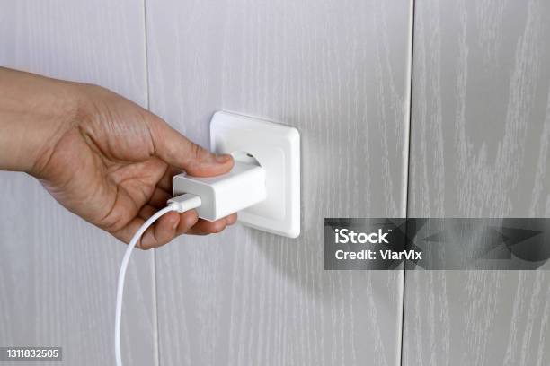 Hand Turns On Turns Off Charger In Electrical Outlet On Wall Stock Photo - Download Image Now