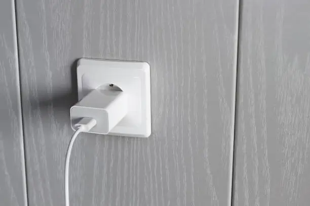 Charger power supply is connected to electrical outlet on wall with copy space