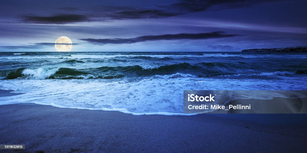 sea tide on a cloudy night sea tide on a cloudy sunrise. green waves crashing golden sandy beach in full moon light. storm weather approaching. summer holiday concept Sea Stock Photo