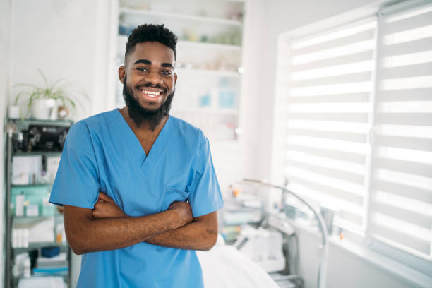 a smiling therapist with his arms crossed standing in his clinic - exfoliating scrub imagens e fotografias de stock