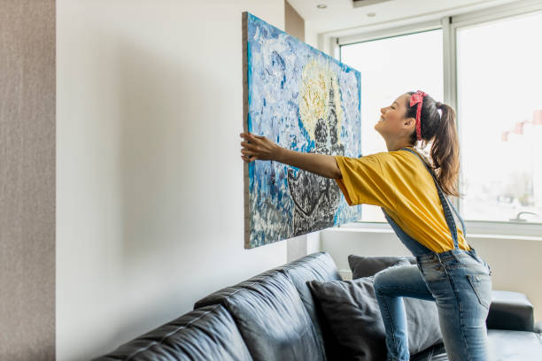 молодая женщина висит художественная картина на стене и украшения гостиной - home decorating фотографии стоковые фото и изображения