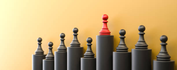 Leadership and growth concept, red pawn of chess, standing out from the crowd of black pawns, on yellow background with empty copy space stock photo