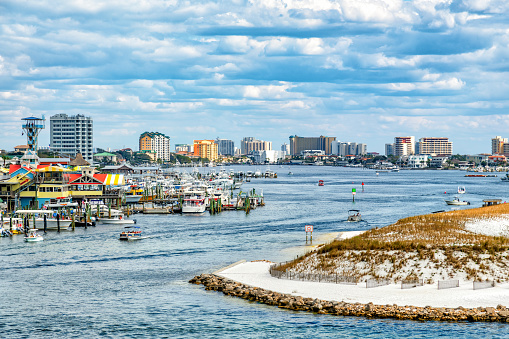 A beautiful white sand beach along Destin Harbor  with the town's skyline in the distance along the Gulf Coast of Florida on a warm spring day.