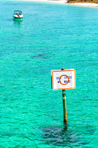 A warning sign advising boaters to slow to not generate a wake in the shallow waters of Destin Harbor along the Gulf Coast of Florida.